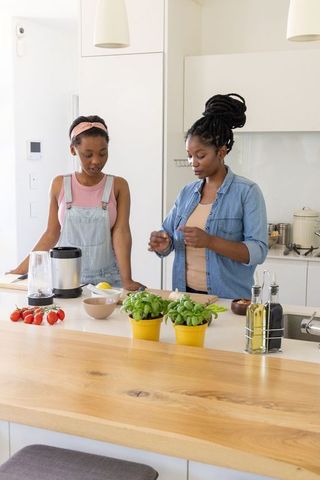 African american mother and teenage daughter cooking together in bright modern kitchen