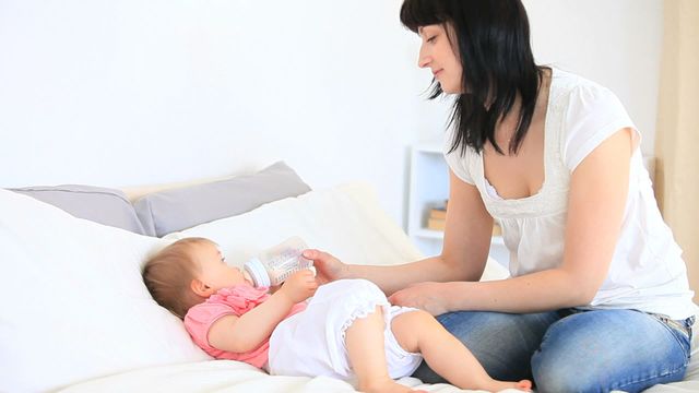 A mother is bottle-feeding her baby in a comfortable bedroom environment. This setting perfectly captures a nurturing moment, emphasizing the bond between parent and child. Ideal for use in parenting blogs, parenting magazines, advertising for baby products, or informational content about infant care.