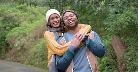 Couple hugging and laughing on forest trail wearing beanies and cozy knitwear