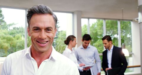 Smiling Businessman with Team Meeting in Background