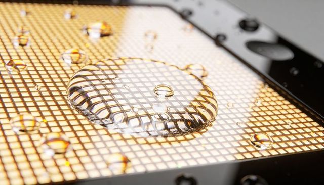 Refracting water droplet casting grid reflections on backlit panel macro close-up