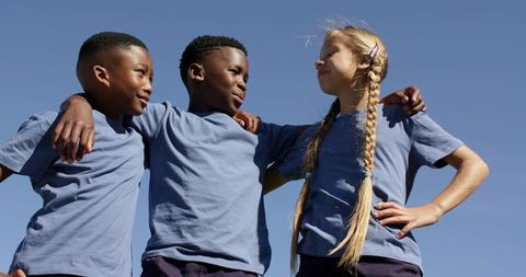 Preteen diverse kids linking arms outdoors smiling teamwork friendship unity under blue sky
