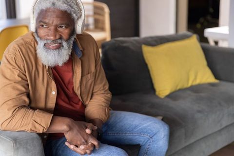 Senior african american man listening with headphones on sofa relaxing at home
