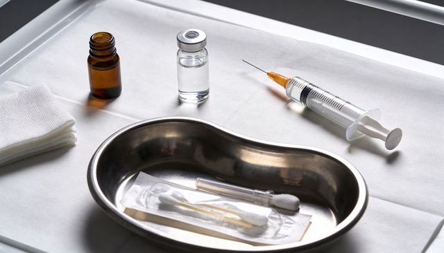 Sterile medical tray holding syringe, vial, gauze and wrapped cotton swabs on clinic drape