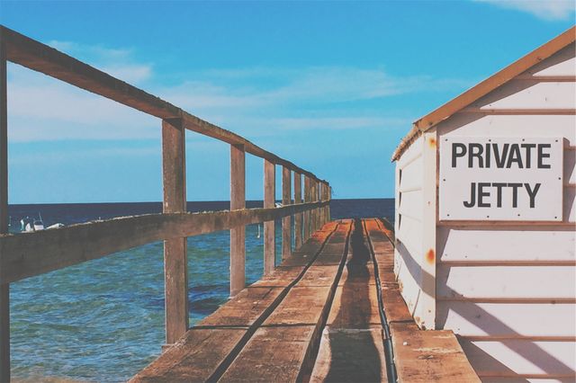 This image features a wooden private jetty stretching into a calm turquoise sea under a clear sky. It can be used for travel advertisements, vacation brochures, websites promoting coastal destinations, and serene oceanfront experiences.