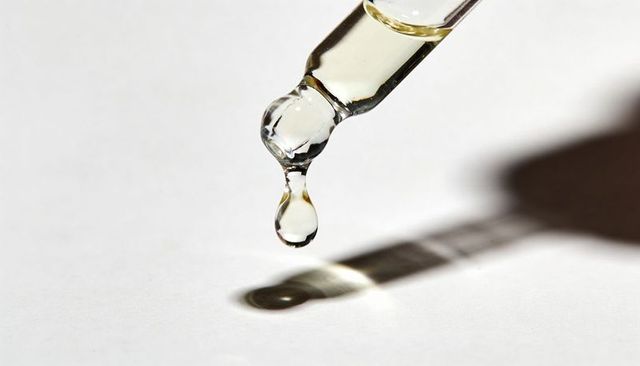 Macro glass dropper releasing clear liquid droplet casting crisp shadow and reflective highlights