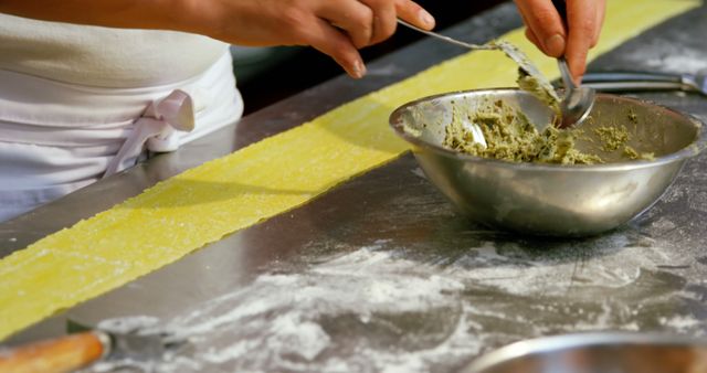 This image explores the hands of a person preparing fresh pasta with a pesto filling, creating an inviting culinary scene. Ideal for use in cooking blogs, recipe websites, culinary magazines, or food product advertisements to highlight homemade cooking and authentic Italian dishes.