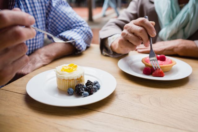 Senior couple having cupcake with blueberries and blackberries in outdoor cafÃ©