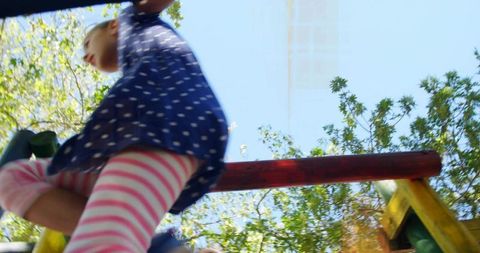 Low-angle child climbing playground bars wearing polka-dot dress and pink striped leggings