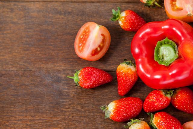 This vibrant image showcases fresh red bell pepper, strawberries, and tomato halves on a wooden table, emphasizing healthy eating and organic produce. Ideal for use in articles, blogs, or advertisements related to nutrition, vegetarian or vegan diets, farm-to-table concepts, and natural food promotions.
