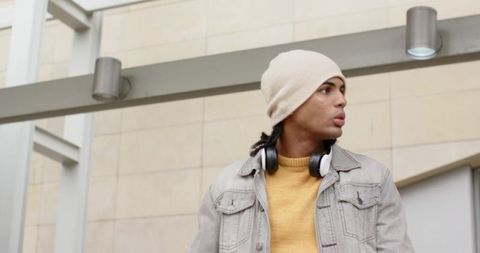 Young man wearing beanie and headphones standing in modern transit concourse, denim jacket