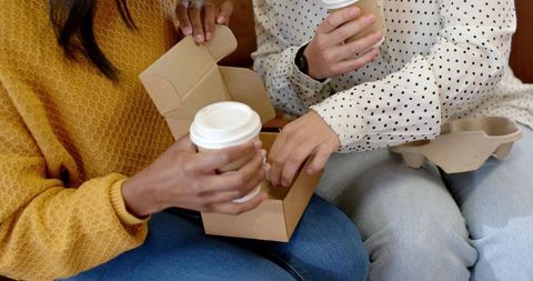 Diverse friends sharing takeaway coffee on bench, holding cardboard box and to-go cups