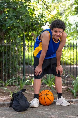 Teen athlete pausing after outdoor basketball session on sunlit park path with backpack