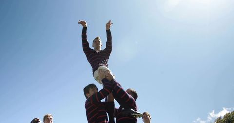 Rugby line-out hoisting jumper skyward team lifting drill under blue sky with lens flare
