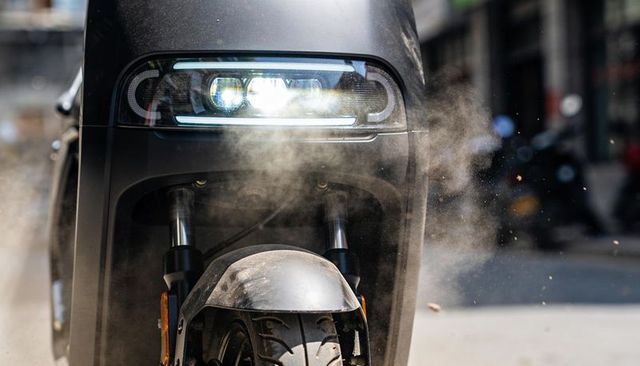 Close-up matte black electric scooter front lighting led headlight kicking up urban dust