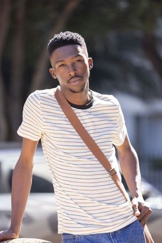 Young african american man leaning on ledge with crossbody bag in urban daylight