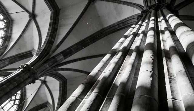 Gothic column rising toward ribbed vaulting with dramatic light and deep shadows