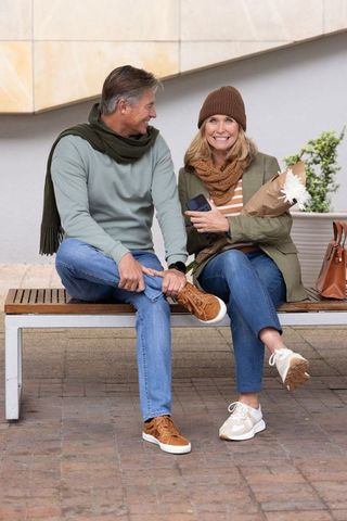 Senior couple sitting on bench holding bouquet and smartphone smiling during urban outing