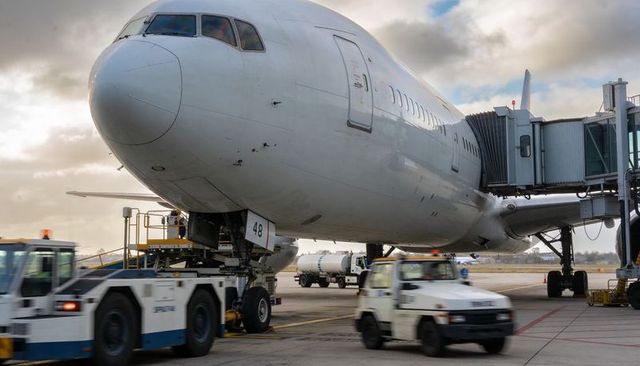 Wide-body airliner docking at gate with boarding bridge, pushback tug and refueling truck