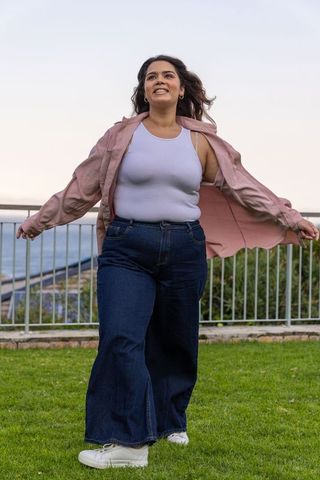 Confident woman walking waterfront smiling in pink overshirt white tank and wide-leg jeans