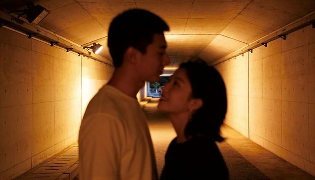 Amber tunnel romance: young couple standing face-to-face under warm urban lights