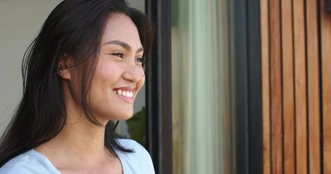 Asian woman smiling by sliding door showing multiple ear piercings lifestyle portrait