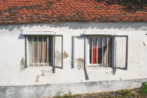 Aged White Cottage Wall Featuring Open Shutter Windows under Red Tiled Roof, Peeling Plaster