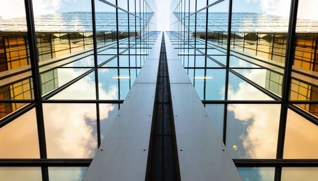 Drawing eye upward through central column and reflective glass facade with sky reflections