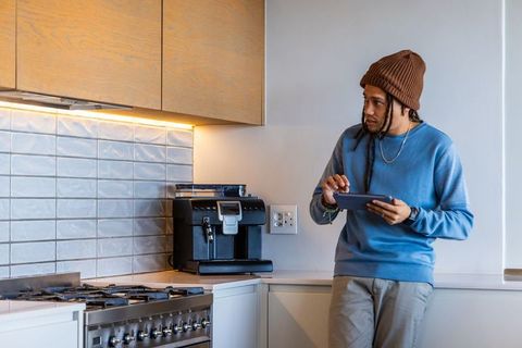 African american man using tablet in modern kitchen near espresso machine and gas range