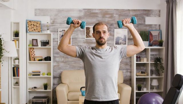 Man lifting dumbbells in living room home workout with kettlebell and exercise ball