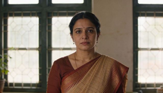 Middle-aged indian woman standing in office wearing beige sari by tall windows, looking at camera