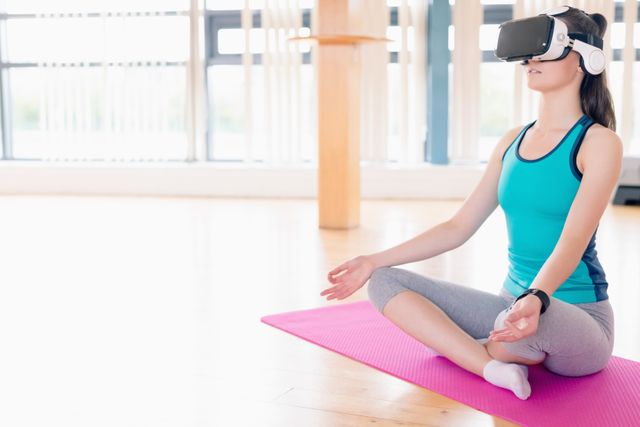 Woman performing yoga while using virtual reality headset in the gym