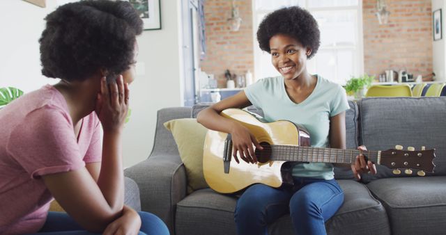 Happy african american mother and daughter sitting on sofa playing guitar - Download Free Stock Photos Pikwizard.com