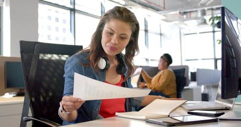 Diverse woman reviewing report at modern open-plan office desk with laptop