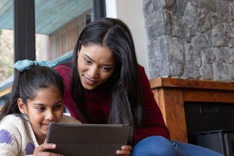 Asian mother and daughter bonding over tablet in cozy living room, learning together