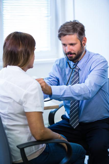 Male doctor using stethoscope to examine patient in hospital setting. Ideal for healthcare, medical consultation, patient care, and professional medical services themes.