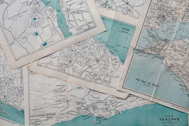 Collection of vintage maps overlapping on table, ideal for historical research, travel blogs, educational purposes, or decor. Suggests adventure, exploration, studying map techniques, or geographic themes. Can be used in articles about history, navigation, or travel planning.