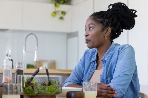 African-american woman enjoying relaxed breakfast in modern kitchen with salad and juice