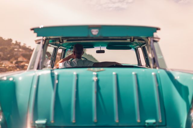 Vintage turquoise car on road trip with driver relaxing inside, enjoying scenic coastal view. Ideal for travel, adventure, transportation, and lifestyle content. Great for blogs, advertisements, and social media posts about retro auto nostalgia.