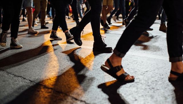 Nighttime crosswalk crowd walking feet casting dramatic shadows on city asphalt