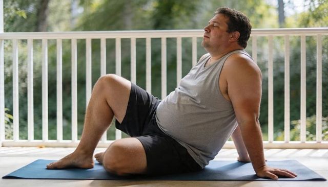 Plus-size man stretching on porch mat on sunny balcony practicing gentle fitness