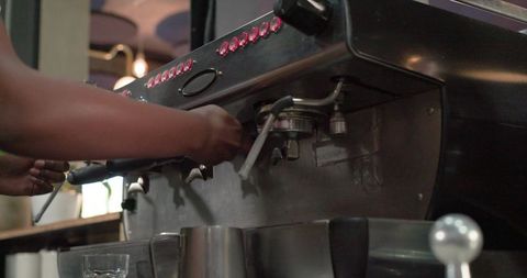 African female barista preparing espresso with portafilter on stainless steel machine
