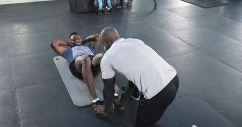 Personal Trainer Guiding Client in Sit-Up Exercise in Fitness Gym