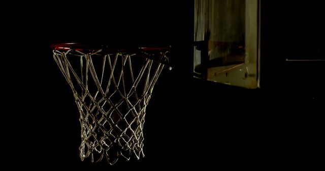 Basketball net and hoop captured in a dark setting with low lighting, emphasizing the metallic textures and the empty net. Ideal for sports ads, motivational posters, and basketball-related content.