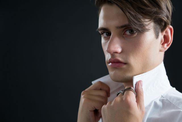 Portrait of androgynous man holding his collar against black background