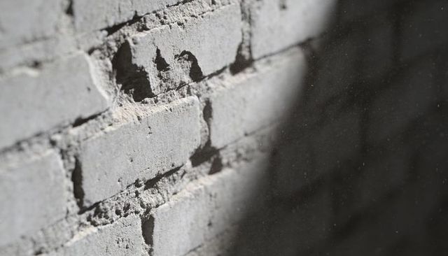 Weathered pale gray brick wall with chipped mortar, diagonal shadow and floating dust