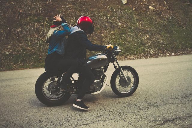 Two bikers are riding a motorcycle on a road with helmets and casual clothing. The focus is on the rear view, highlighting the sense of adventure and freedom. This image can be used for travel blogs, motorcycle gear advertisements, or articles promoting road safety.