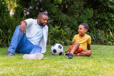 African american father and son sitting on lawn with soccer ball playful backyard bonding