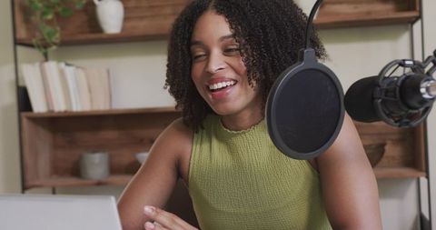 Smiling female podcaster recording at home studio with laptop microphone and pop filter