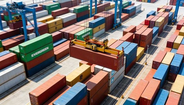Aerial container terminal with crane lifting red container over stacked multicolored cargo